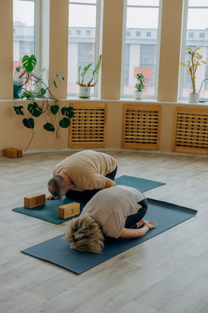 services-02 Two adults practicing yoga in a serene indoor setting, focusing on relaxation and wellness.